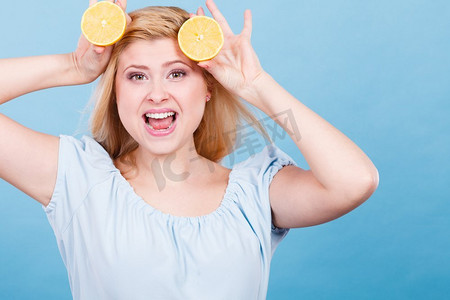 一个微笑的少女，手里拿着两半黄色的柠檬柑橘，蓝色的。健康饮食营养..拿着柠檬柑橘水果的女孩