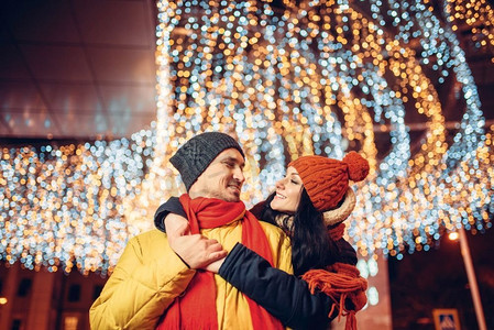冬日浪漫摄影照片_冬日的傍晚，微笑的情侣在街上拥抱。男人和女人有浪漫的会议，幸福的关系