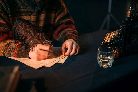 深蓝色背景复古摄影照片_男性的手用羽毛在老式纸上写字。深蓝色桌布背景。男性的手用羽毛在老式纸上写字