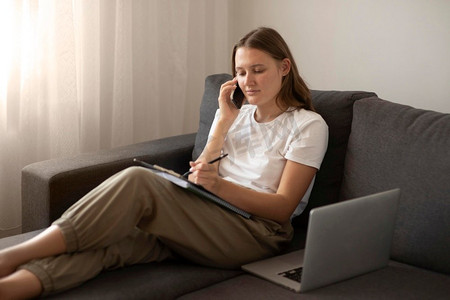 妇女在隔离期间工作的家庭沙发与智能手机笔记本电脑