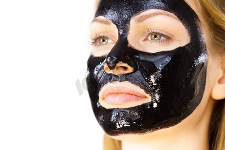 对面膜摄影照片_年轻女子与化妆品在脸上，碳水化合物排毒黑色剥离面膜。水疗护理。护肤品妇女与黑色剥离关闭面具在脸上