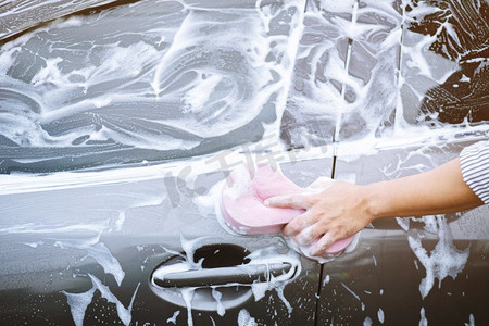 一名男子手持粉色海绵洗车。概念洗车干净。