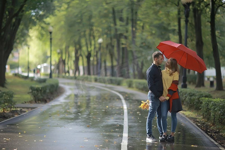 秋天公园里的雨/25岁的年轻夫妇在雨天打伞散步，十月情侣