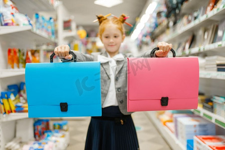 在文具店拿着两个文件夹的小女生。女童在商店购买办公用品，学生在超市