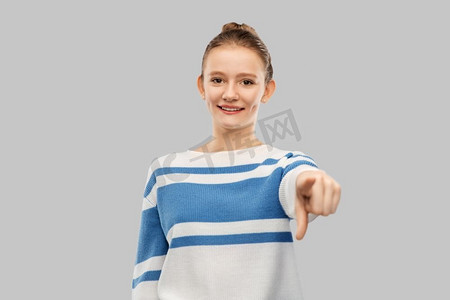 手势和人物概念-穿着套头衫的十几岁女孩微笑着，在灰色背景下用手指指着相机。微笑的少女指着相机