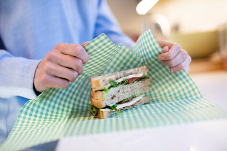 环保食品摄影照片_特写妇女包裹三明治在可重复使用的环保蜂蜡包裹