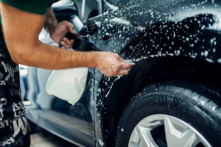 工人分散肥皂水，准备汽车防止碎屑和划痕。油漆保护。保护涂层