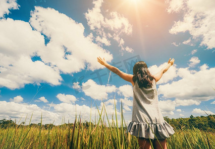 夏日免费摄影照片_夏日，青草草地上的年轻美人向蔚蓝阳光灿烂的天空张开双臂。度假和冥想的概念。