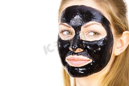 年轻女子脸上涂着化妆品，碳水化合物排毒黑脱口罩。水疗中心。护肤品..脸上戴着黑色口罩的女子
