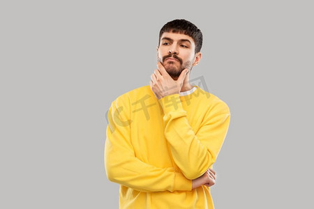 人的概念—年轻人在黄色运动衫思考灰色背景。穿着黄色运动衫的年轻人