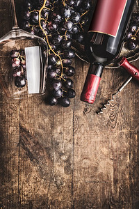 红葡萄酒瓶和玻璃与葡萄在乡村木背景。俯视图。边境复制空间。品酒理念