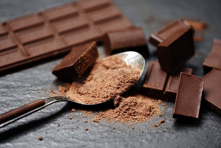 甜摄影照片_巧克力棒和巧克力粉在勺子在黑暗背景/块糖果甜的甜点和小吃