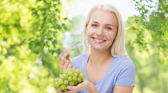 健康的饮食，食物，饮食和人的概念—愉快的微笑的妇女吃葡萄在绿色自然背景。吃葡萄的快乐女人