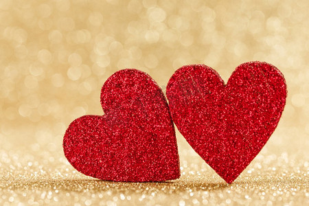 两个小手工制作的红色闪光心脏在明亮的金光bokeh背景情人节卡。两颗心在散景背景