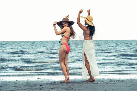 暑假里，穿着比基尼的快乐女人们在热带沙滩上一起跳舞。旅行生活方式..快乐的女人在夏天的沙滩上跳舞。