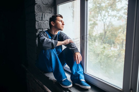 一个抑郁的男人坐在窗台上在黑暗的房间，精神病患者。精神病患者的观念，强调人，抑郁症