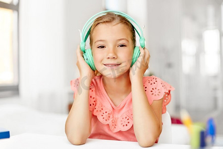 儿童和技术的概念—在耳机里听音乐的快乐女孩在家庭办公桌。女孩在耳机听音乐在家里