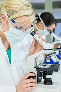 女性医学或科学研究人员，科学家或医生在实验室里使用显微镜，而她的同事在她身后失去焦点。