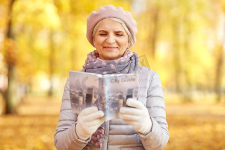 休闲妇女摄影照片_旅行，旅游和退休概念—快乐的老年妇女与城市指南在秋天公园。老年妇女与城市指南在秋季公园