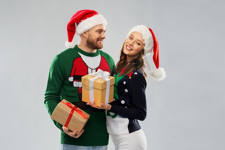 圣诞毛衣摄影照片_人和假日概念—在丑陋的毛衣聚会圣诞老人帽子的快乐夫妇。快乐的夫妇在圣诞毛衣与礼物
