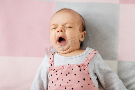婴儿期和人的概念-甜蜜的打哈欠小女孩穿着粉色西装躺在针织毯子上。穿着粉色西装的打哈欠的女婴躺在毯子上