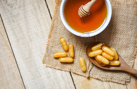 胶囊胃镜摄影照片_蜂王浆胶囊在木汤匙在袋背景和蜂蜜在杯子/黄色胶囊药物或补充食品从自然健康
