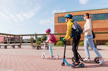 教育，学校和家庭概念—快乐的女儿，儿子和母亲骑滑板车户外。快乐的学生与母亲骑滑板车