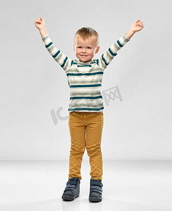 童年，成功和人的概念—愉快的小男孩条纹衬衫与举起手在灰色背景。快乐的小男孩举起双手