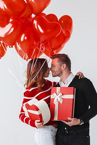气球浪漫背景摄影照片_拿着情人节礼物和红色气球在白色背景的愉快的微笑的夫妇。情人节夫妇与礼物