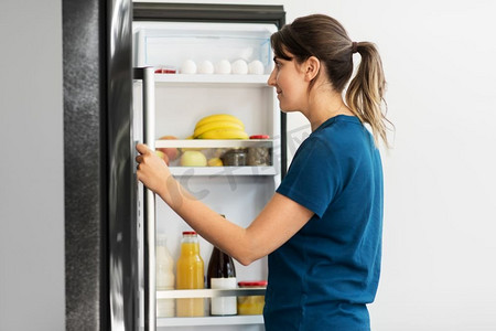 健康饮食，食物和饮食概念—快乐的女人在开放冰箱在家庭厨房。快乐的女人在打开冰箱在家里厨房