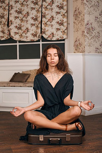 年轻女子冥想在一个手提箱瑜伽姿势。复古风格的客厅在背景。年轻女子坐在一个姿势瑜伽在手提箱上。