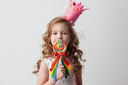 美丽的小糖果公主女孩在冠拿着大棒棒糖和微笑。女孩在皇冠拿着棒棒糖