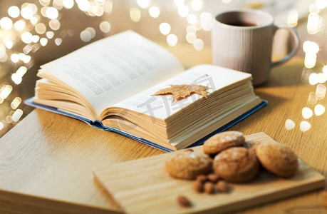 hygge和舒适的家庭概念书与秋天的叶子，一杯茶和燕麦饼干在木桌上。桌上有秋天的叶子、饼干和茶的书