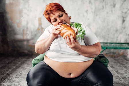 胖女人坐在椅子上吃三明治，暴食症和超重。不健康的生活方式，肥胖。胖女人坐在椅子上吃三明治，暴食症