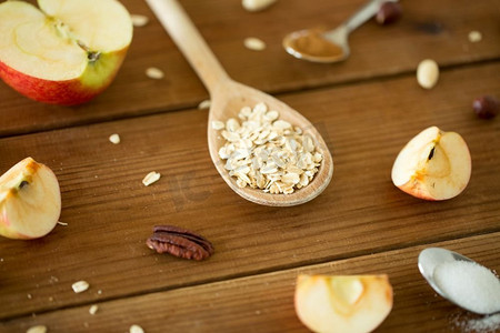 食物烹饪和饮食概念-燕麦片放在勺子里，切好的苹果和坚果放在木桌上。木勺燕麦片，切好的苹果和坚果