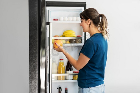 健康饮食，饮食和饮食理念-快乐的女人从家里厨房的冰箱里拿葡萄柚。快乐的女人在家里从冰箱里拿食物