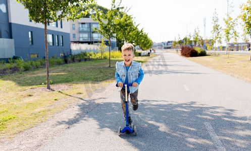 童年，休闲和乐趣的概念—快乐的小男孩骑滑板车在城市。快乐的小男孩骑摩托车在城市