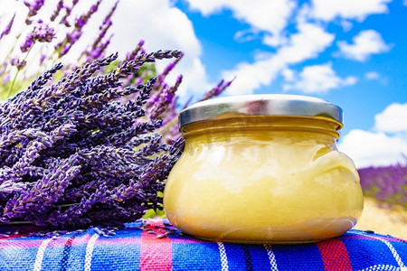 熏衣草摄影照片_与蜂蜜的罐对新鲜熏衣草领域背景。法国普罗旺斯一罐蜂蜜和熏衣草花。