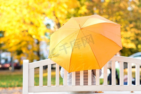 季节、雨天和人的概念秋季公园里打伞的女人坐在长凳上。秋日公园，一位撑着伞的女子坐在长凳上