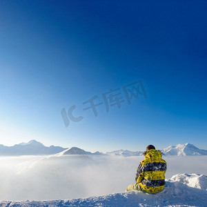 雪摄影照片_高山冬季山风景与人坐在低云之上。法国阿尔卑斯山在晴天被雪覆盖。Val—d Isere’