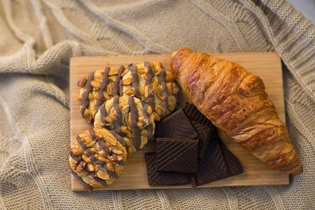 食物，饮食和早餐的概念—羊角面包，巧克力块和饼干在木板。牛角面包，巧克力和饼干在木板上