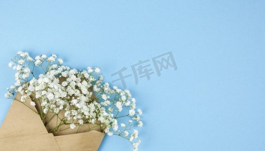 棕色信封与小白色的gypsophila花安排角落蓝色背景 