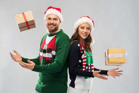人和假日概念—在丑陋的毛衣聚会圣诞老人帽子的快乐夫妇。快乐的夫妇在圣诞毛衣与礼物
