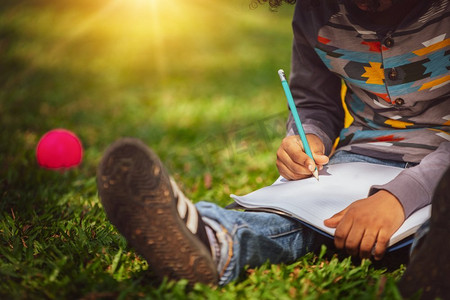 日文手写摄影照片_在一本笔记本上写的小孩子小学生，当坐在绿色的草地在公园。儿童教育理念。
