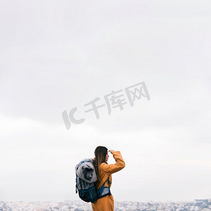 侧面视图年轻女性徒步旅行者与她的背包俯瞰城市风景反对天空