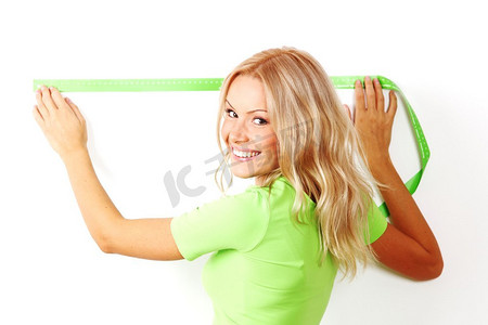 年轻美丽的微笑的妇女测量间隔在一面墙与绿色测量带，白色背景。妇女测量间距在墙上