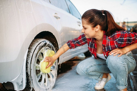 可爱的女人与海绵擦洗车轮泡沫，洗车。女士自助洗车。夏日户外洗车 