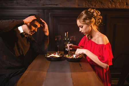 年轻夫妇在餐馆争吵，晚上不好。优雅的女人在红色礼服和她的男人吃在咖啡馆