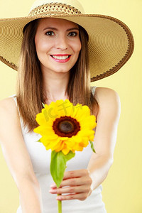戴花的美女摄影照片_黄色背景下手持向日葵、头戴草帽的夏日美女特写