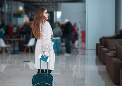 拖着行李箱的人摄影照片_年轻的女旅行者在机场大厅拖着行李。机场咖啡馆背景。适用于公交、铁路、地铁站。